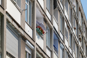 Generic old grey concrete communist era apartment block facade, balconies detail. One balcony with red flowers and striped awning, individuality concept residential architecture, urban density, nobody