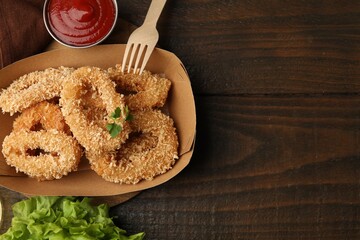Deep fried squid rings with parsley in takeaway paper box, lettuce and ketchup on wooden table, flat lay. Space for text