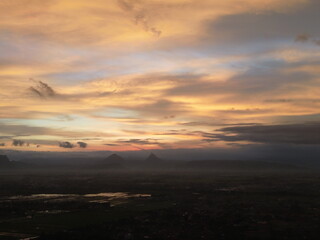 Wide sunset landscape with glowing clouds above distant mountains and fields. Warm atmospheric colors create a dramatic and peaceful skyscape.