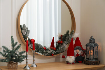 Mirror, burning candles and Christmas decor on console table near white wall indoors
