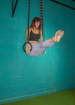 Gymnast performs an L-shaped seated position on rings, lifting her legs forward and supporting her body with extended arms