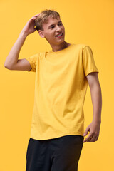 Smiling young male in a bright yellow t shirt standing against a vivid yellow background, casual...