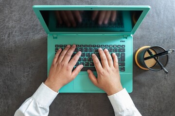 A man's hands working on a green laptop, aerial view