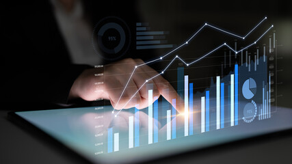 A business professional engages with a digital tablet displaying interactive charts, presenting insightful data for analysis and decision-making in a corporate environment. Scalp