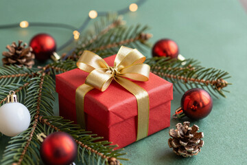 Festive red gift box with golden ribbon, surrounded by lush fir branches, shiny ornaments, and natural pinecones, evoking the joy of holiday celebrations and winter cheer
