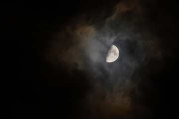 Obraz premium Bright half moon shining through dark spooky clouds in night sky astronomy concept