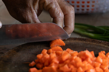 Close up hands of man chopping fresh orange carrots on wooden cutting board cooking preparation