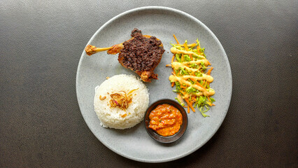 Overhead shot of crispy black-seasoned fried duck (Bebek Goreng) served with white rice, fresh vegetable salad, and spicy Indonesian chili sauce (Sambal). Concept for Asian food, cuisine.