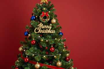 Festive Holiday Christmas Tree Adorned with Lights and Ornaments Against a Warm Red Background, Symbolizing Seasonal Joy and Celebration