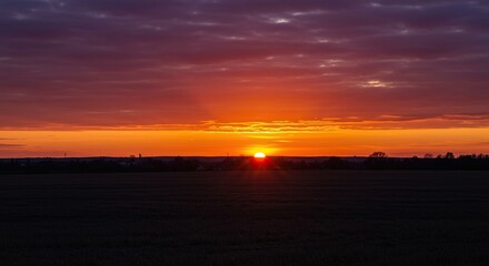 A breathtaking, wide vista showcasing the sky ablaze with intense orange, purple, crimson, and golden hues as the giant sun dips below the distant horizon line ,sky ,twilight ,serene