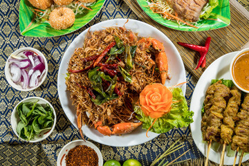 Thai food platter with crab claws, noodles, grilled meat, fish fillet, and coconut balls.