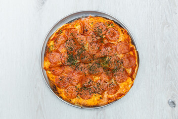 Pepperoni pizza with herbs and cheese served on a round tray with golden crust.