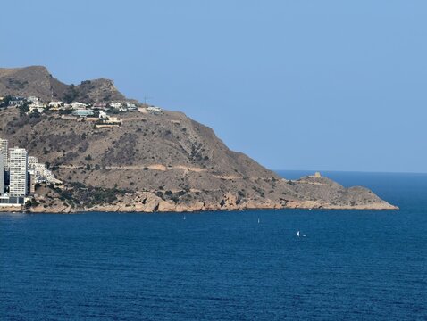 picturesque hillside village on sunlit coastline overlooking serene blue sea and rocky shore