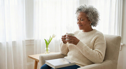 Content senior Black woman relaxes in an armchair with a steaming mug, enjoying a peaceful moment at home by a bright window.