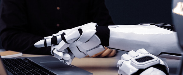 A futuristic robotic arm points towards a laptop, highlighting the blend of advanced technology and human-like interaction in a modern workspace setup.Noogenesis