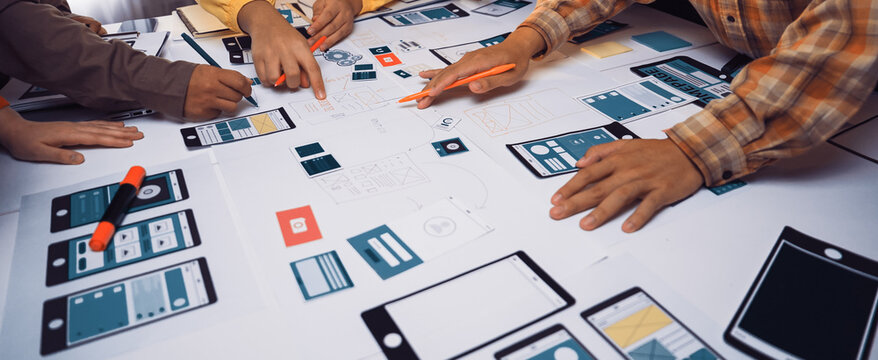 A vibrant workspace filled with professionals engaged in a collaborative design session. Hands draw and discuss mobile app prototypes and sketches, showcasing creativity and teamwork. SACTR - Powered by Adobe