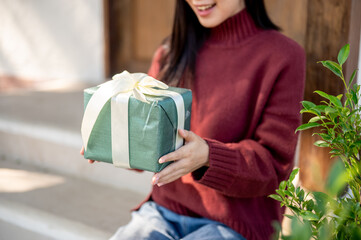 Close up woman in red sweater holding at present gift box while sitting in front of home cafe's door