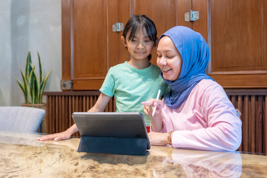 Indonesian hijab woman and daughter are looking at a tablet. They are discussing something while reading and working in a cafe.