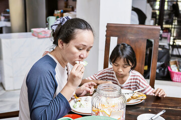 Indonesian woman and a child are having meal in dining table. They are enjoying the food while eating together