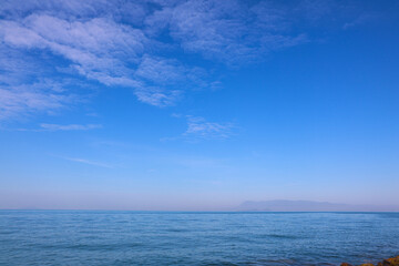 Fototapeta premium Vast Calm Ocean Horizon Under Deep Blue Sky with Wispy White Clouds and Distant Mountains