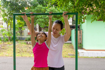 Fototapeta premium A happy Indonesian woman is helping a young girl to hang from a bar