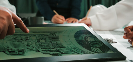 A diverse team collaborates, analyzing a detailed technical blueprint in a modern workspace setting. Various tools and discussions illustrate effective engineering practices. SACTR