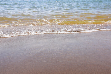 Close-up view of gentle wave washing onto brown beach sand texture background
