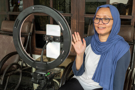 Indonesian hijab woman is waving to the camera and doing livestream for selling at home.