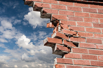 Brocken brick wall and blue sky with white clouds on background