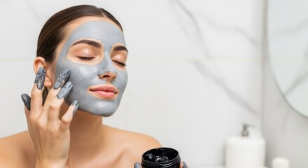 A woman applying a gray facial mask with her fingers in a bright bathroom with eyes closed relax