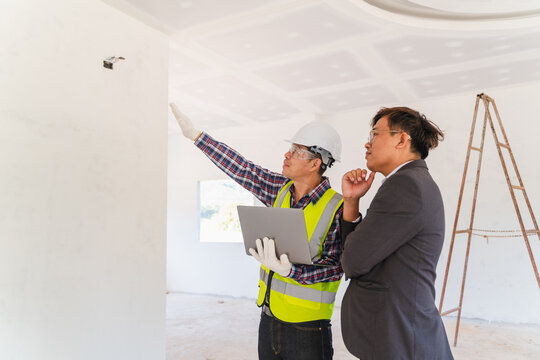 Two men discussing construction progress in a modern building site with white walls, one in safety gear and the other in a suit, assessing work quality and planning.