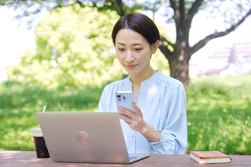 屋外でスマートフォンとノートパソコンを使う女性