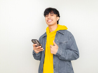 Smiling young man holding a smartphone and giving a thumbs up gesture, ideal for technology ads, mobile apps, digital communication, social media content, and modern lifestyle themes.