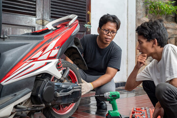 Indonesian southeast asian repairman with a green impact wrench tool discusses replacing the part with his customer after examining a motorcycle in a workshop