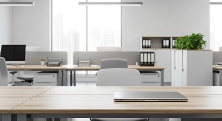 A laptop on a wooden desk in a modern office with a city skyline visible through the windows.