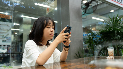 A young girl using a smartphone while sitting at a table indoors.