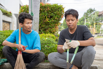Two Indonesian southeast asian gardeners men sitting and resting while talking after doing some gardening in the backyard. Gardening work