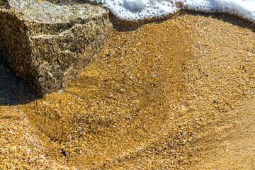 Sand rocks pebbles mussels shells waves Kalim Beach Phuket Thailand.
