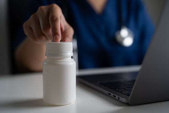 Doctor in blue scrubs interacting with medication bottle during virtual consultation, showing telehealth, modern medical technology, remote care services, and digital health monitoring system.