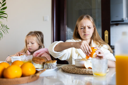 two sisters peeling an orange together at kitchen table, sharing activity during breakfast time