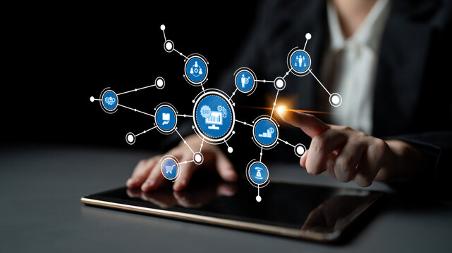 A professional hand interacts with a digital tablet displaying intricate network connections and business icons, symbolizing modern technology and communication innovations. Tessel - Powered by Adobe