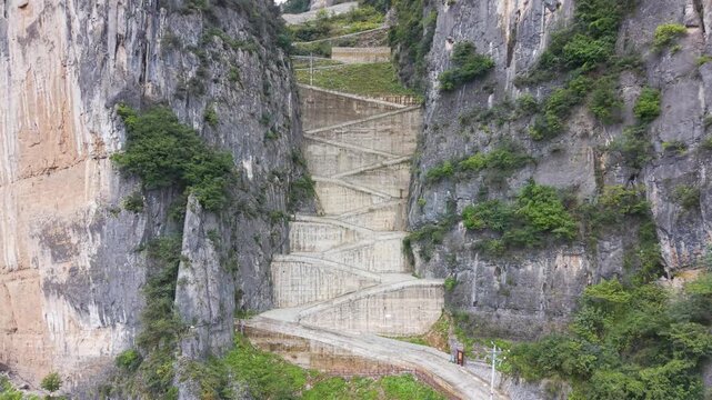 Top-down aerial view of the steep, sheer rock formations and the zigzag road carved into the cliffside at Lingpaishi, Wuxi County, China. Captures remote natural beauty and engineering. UHD.