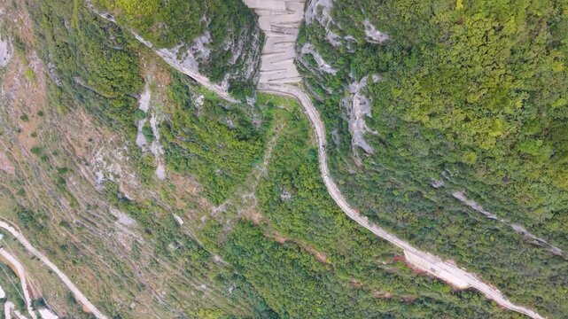 Top-down drone shot of the steep, sheer rock formations and the zigzag road carved into the cliffside at Lingpaishi, Wuxi County, China. Captures remote natural beauty and engineering. UHD.