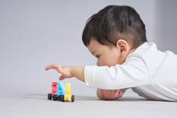 The child lies prone, extending one arm to touch a toy car at the front of the line.