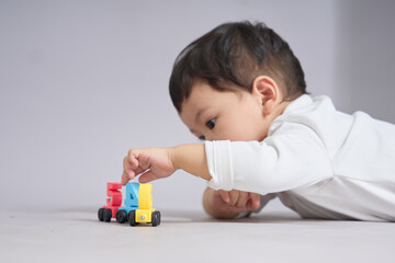 The child lies on the floor, hands arranging several colorful toy cars into a straight line.
