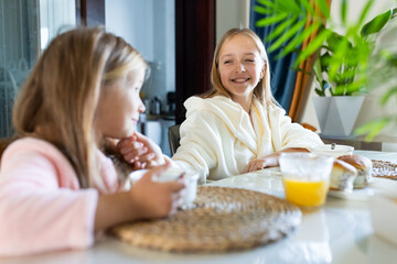 Two young girls enjoying breakfast together in a cozy home setting. teenage girl wiping crumbs from her little sister's face with a napkin after breakfast, caring gesture, family bonding