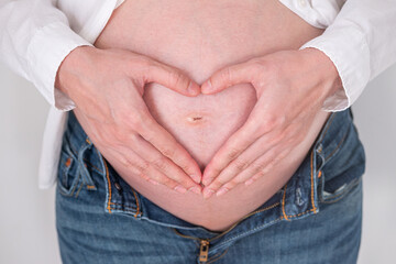 Pregnant woman making heart shape with hands on bare belly close up