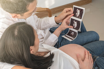 Pregnant couple looking at ultrasound images at home for prenatal bonding