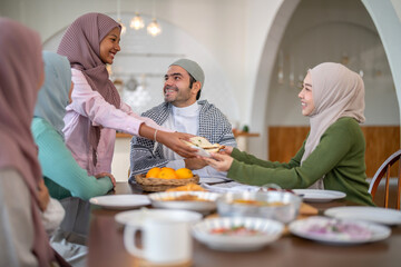 Muslim big family sharing traditional meal together around dining table wearing hijabs and kufi in cultural love, ramadan iftar celebration, eid al-fitr festive, halal meal gathering food culture
