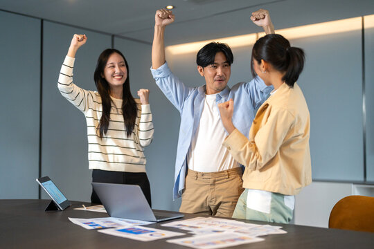 Asian business team celebrating success with raising fist in office, joyful expression teamwork spirit, multicultural collaboration, group achievement, workplace motivation, inclusive company